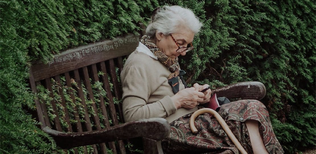 En äldre dam sitter i en soffa och tittar ned i sin mobil